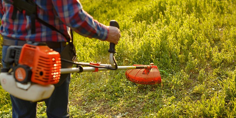 Mann schneidet das Gras an einem Hang mit einem Trimmer