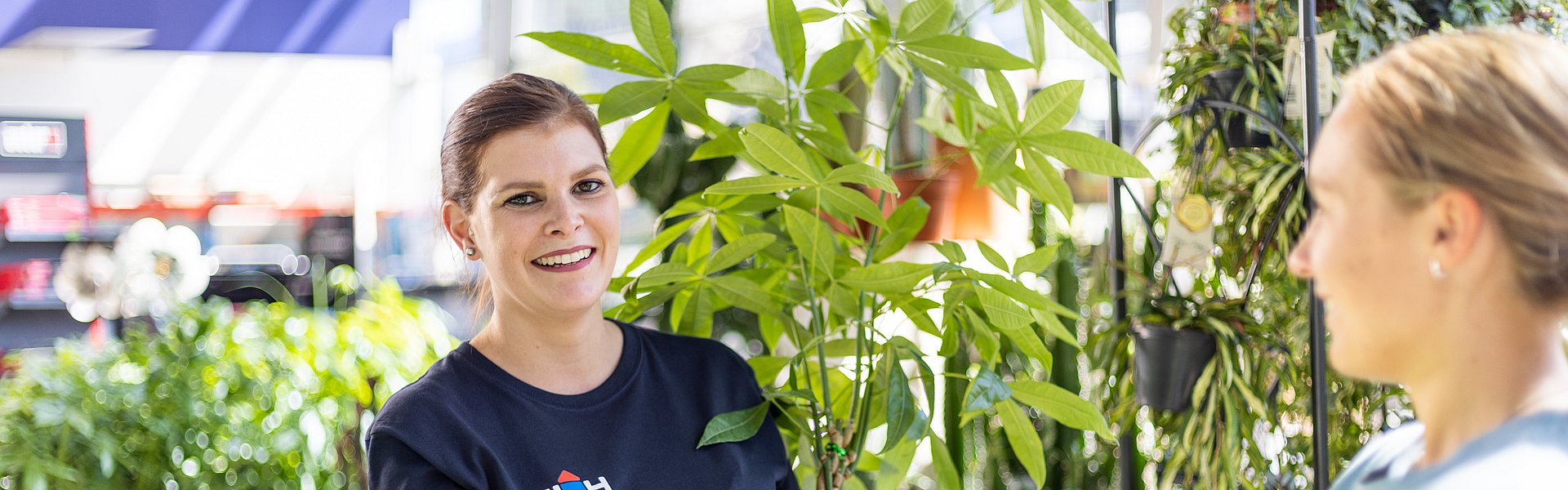 WH Mitarbeiterin im Gartencenter mit Pflanze