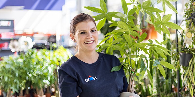 WH Mitarbeiterin im Gartencenter mit Pflanze