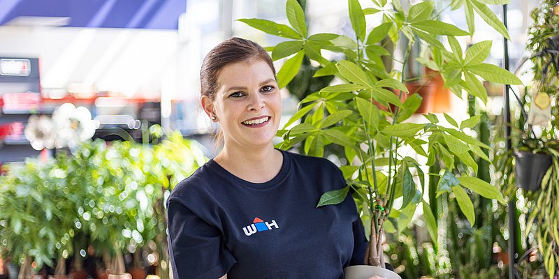 WH Mitarbeiterin im Gartencenter mit Pflanze