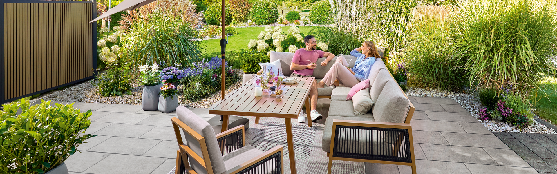 Zwei Personen sitzen an einem sonnigen Tag im Garten auf der Terrasse und unterhalten sich