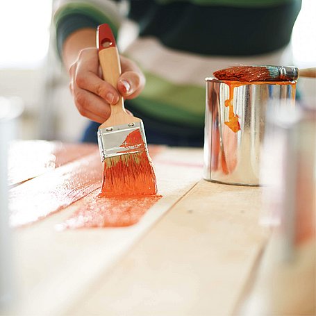 Person streicht Holz mit einer orangenen Farbe