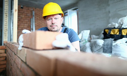 Handwerker mit gelben Schutzhelm zieht eine Ziegelmauer auf