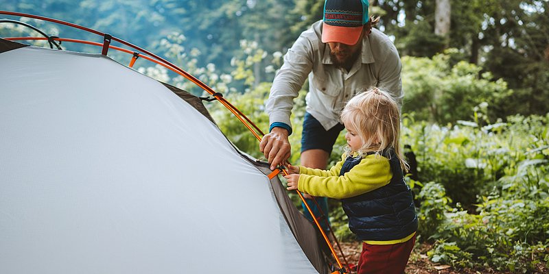 Vater und Tochter beim Aufbauen vom Campingzelt im Wald