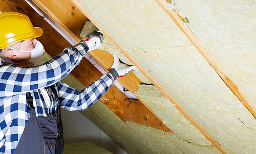 Handwerker verlegt mit Maske Dämmplatten im Dachboden
