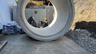 Platzierung eines Stahlbetonrohrs mittels Kran und Arbeiter in Anras