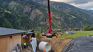 Platzieren eines Betonschachts mittels Arbeiter und Kran in Anras