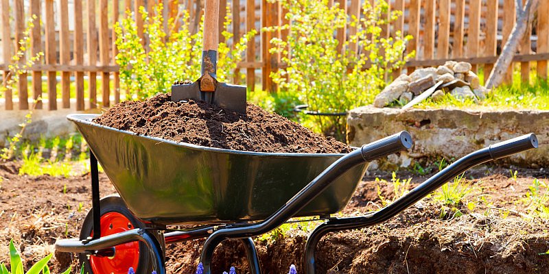 Eine mit Erde gefüllte Schiebtruhe steht im Garten