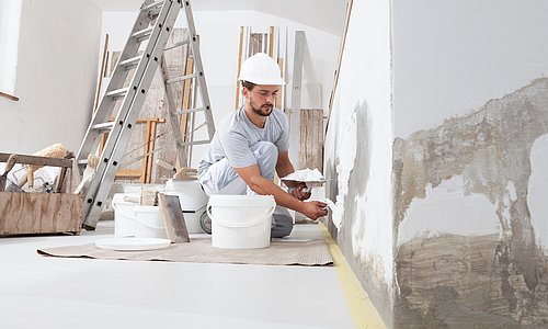 Mann verputzt eine Wand in seiner Wohnung