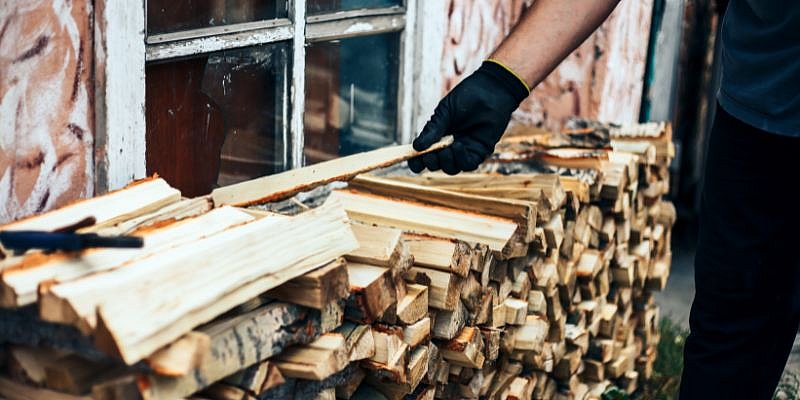 Mann stapelt Brennholz an Hauswand