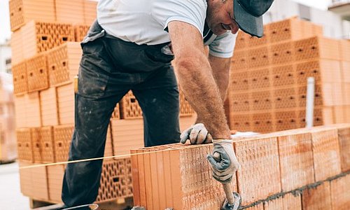 Maurer mit Hammer, Schlagschnur und Ziegeln