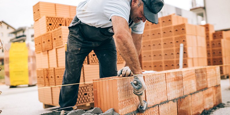 Maurer mit Hammer, Schlagschnur und Ziegeln