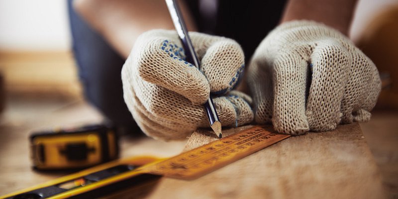 Handwerker zeichnet mit Bleistift und Lineal auf Holz