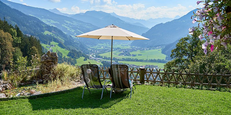 Sonnenschirm und zwei Liegestühle im Garten mit Ausblick ins Tal