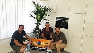 drei Männer mit Würth Hochenburger Werbetafel und grüner Palme