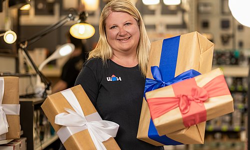 WH Mitarbeiterin hält Geschenk in der Hand weitere befinden sich im Einkaufswagen vor ihr