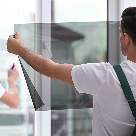 Mann montiert Sonnenschutzfolie auf Fenster