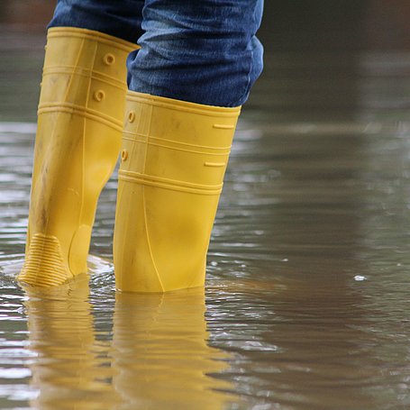 Person steht mit gelben Gummistiefeln im Hochwasser