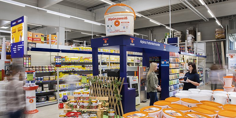 Farbmischservicestation im Baumarkt mit Fokus auf einer Kundin und einer WH-Mitarbeiterin