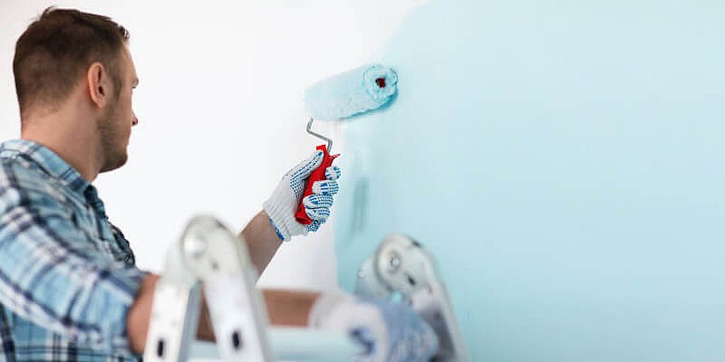 Mann streicht eine Wand hellblau