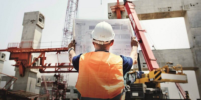 Baumeister mit Helm auf einer Baustelle mit Kran